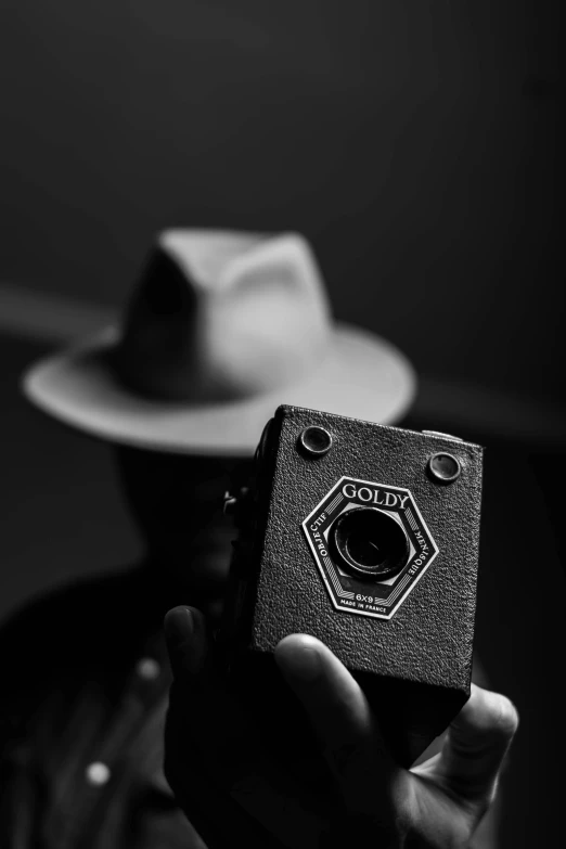 a black and white photo of a man holding a camera, inspired by Louis Faurer, unsplash, noir detective and a fedora, abstract claymation, medium format, !!! colored photography