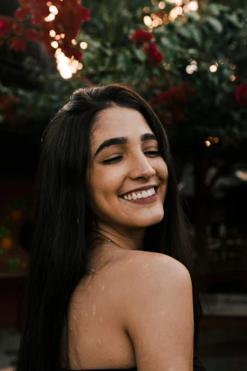a woman with long black hair smiling at the camera, trending on pexels, happening, showing her shoulder from back, non binary model, brown smiling eyes, young woman in her 20s
