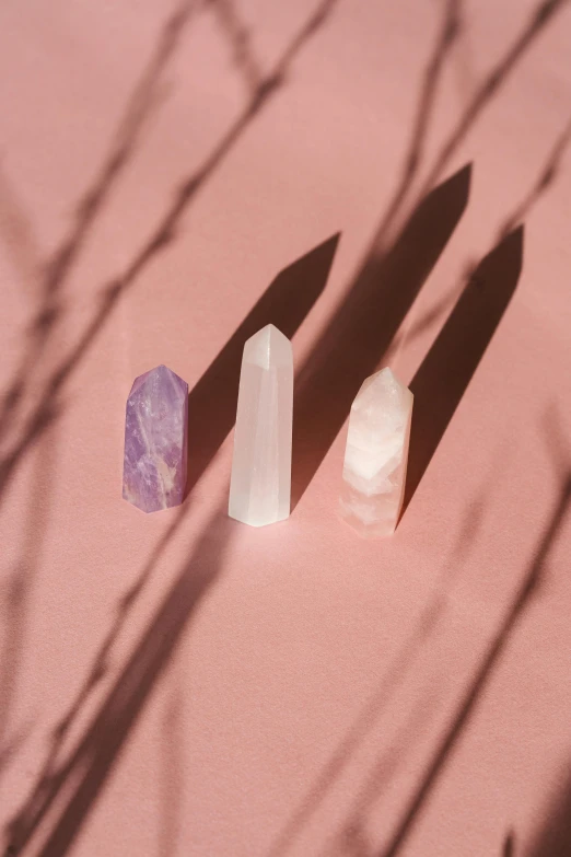 a couple of crystals sitting on top of a pink surface, a marble sculpture, trending on pexels, obelisks, the three moiras, white and purple, medium long shot