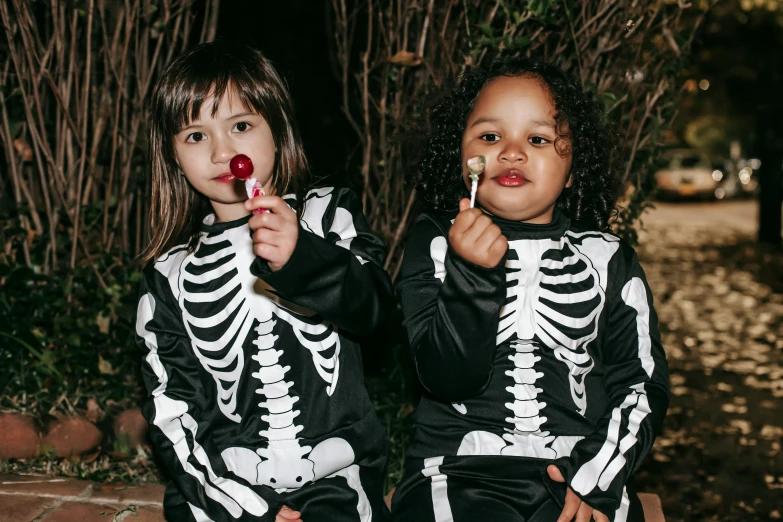 two little girls dressed up in skeleton costumes, unsplash, 💋 💄 👠 👗, cute boys, dark skinned, lollipop