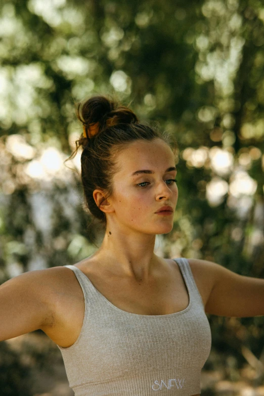 a woman holding a frisbee in a wooded area, pexels contest winner, renaissance, brown hair in two buns, sydney sweeney, figure meditating close shot, she is wearing a black tank top