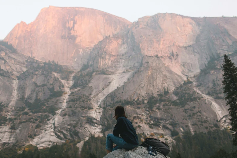 a woman sitting on a rock in front of a mountain, by Marshall Arisman, trending on unsplash, yosemite, profile image, multiple stories, tiny person watching