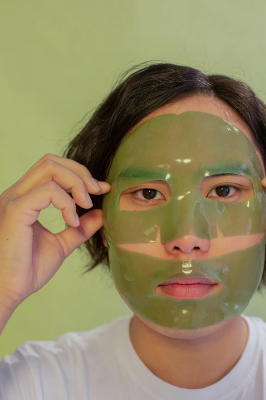 a woman putting a green mask on her face, an album cover, inspired by jeonseok lee, reddit, silicone skin, clear [[bronze]] face [mask], androgynous face, loputyn and matcha