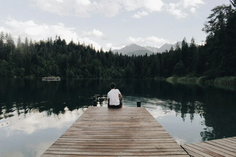 a man sitting on a dock next to a lake, pexels contest winner, tumblr aesthetic, overlooking a vast serene forest, reuniting, slightly minimal