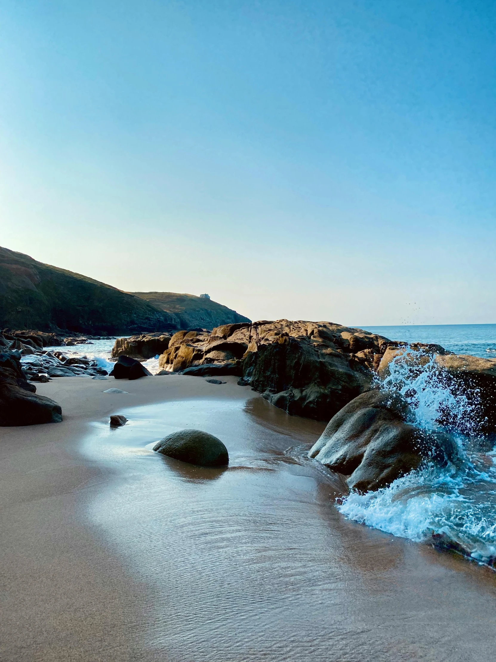 a large body of water sitting on top of a sandy beach, cornwall, rocks, at the golden hour, slide show