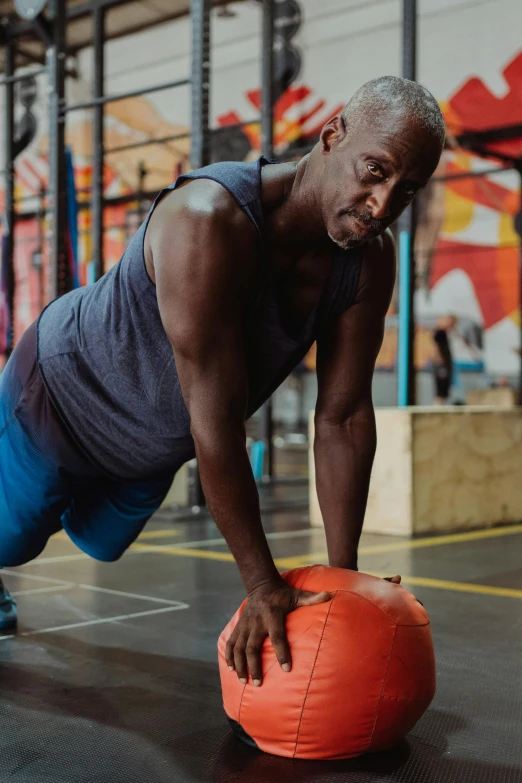 a man doing push ups on an orange ball, by Paul Davis, trending on dribble, lance reddick, in a gym, atiba jefferson, profile image