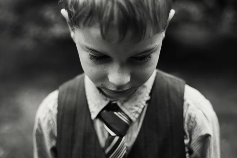 a black and white photo of a young boy wearing a tie, unsplash, medium format. soft light, looking down, portrait shot 8 k, wearing a school uniform