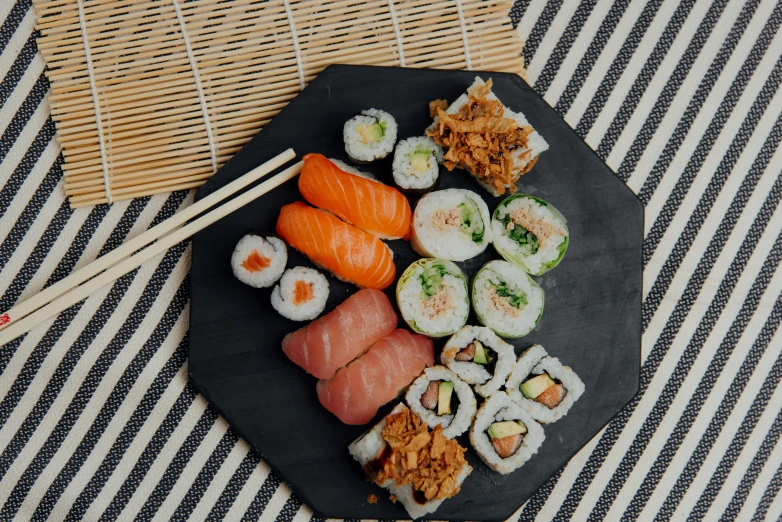 a black plate topped with sushi and chopsticks, inspired by Nishida Shun'ei, trending on unsplash, sōsaku hanga, 🦩🪐🐞👩🏻🦳, 90s photo, 6 pack, on a wooden tray