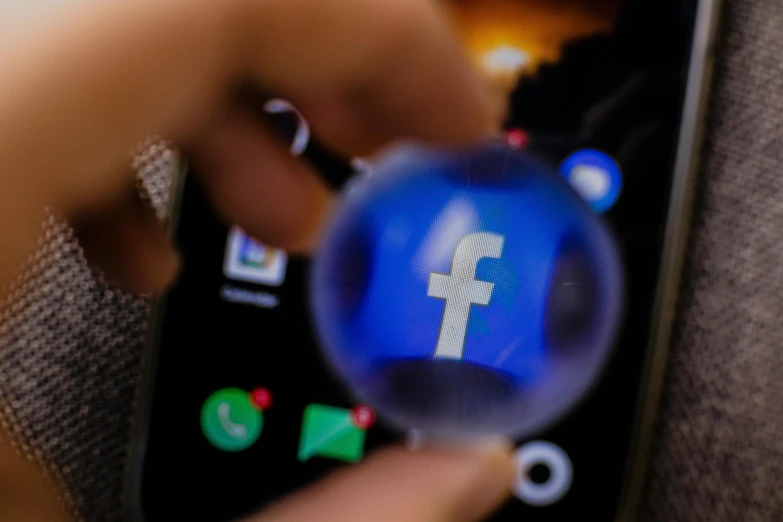 a person holding a glass ball with a facebook logo on it, a picture, by Tom Carapic, trending on pexels, a telephone receiver in hand, 2263539546], a high angle shot, zuckerberg