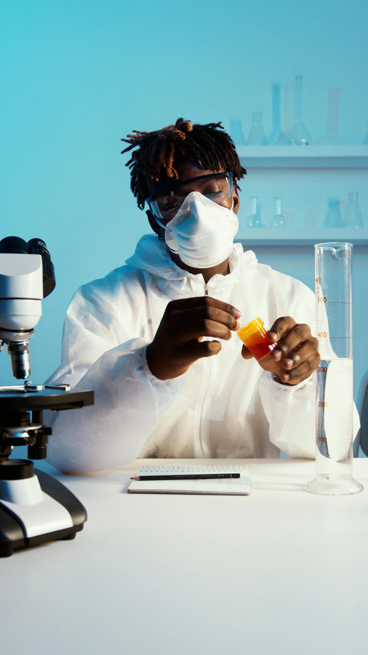 a man sitting at a table in front of a microscope, inspired by Dr. Atl, pexels, afrofuturism, staff wearing hazmat suits, beakers, college, wearing a white hospital gown