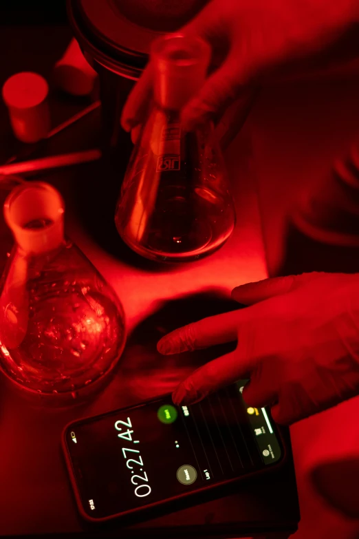 a close up of a person using a cell phone, process art, glowing potions, red light bulbs, handling laboratory equipment, booze