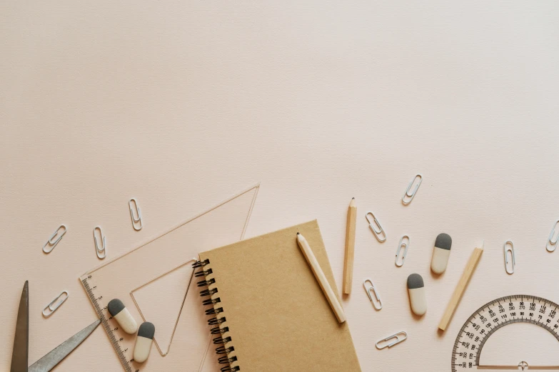 a notebook sitting on top of a table next to a pair of scissors, trending on pexels, academic art, beige colors, pink, made of paperclips, background image