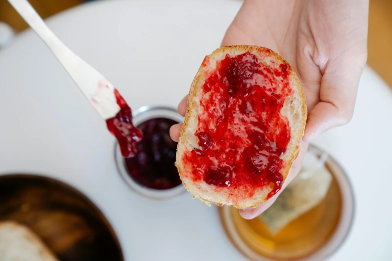 a person holding a piece of bread with jam on it, by Nina Hamnett, pexels contest winner, straya, 🦩🪐🐞👩🏻🦳, jelly, bakery