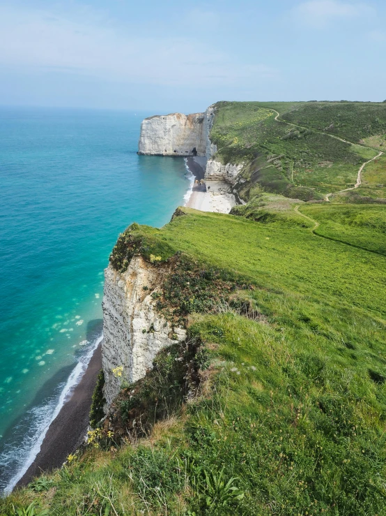 a large body of water sitting on top of a lush green hillside, by Raphaël Collin, pexels contest winner, renaissance, chalk cliffs above, the normandy landings, white shorts and hiking boots, high resolution photograph