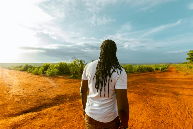 a man with dreadlocks walking down a dirt road, pexels contest winner, afrofuturism, overlooking, man in white t - shirt, sydney park, avatar image