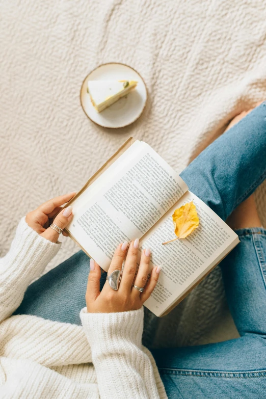 a woman laying on a bed reading a book, trending on unsplash, wearing wheat yellow gauze, wearing a white sweater, sitting on a leaf, eating cheese