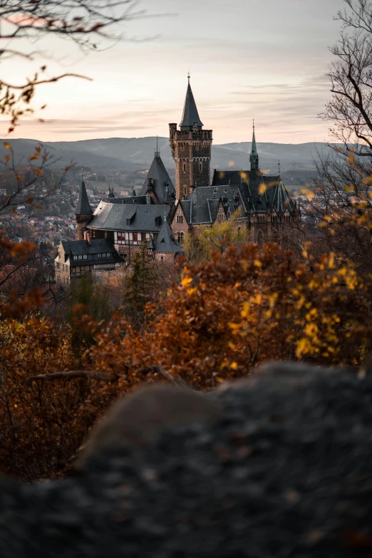 a castle sitting on top of a lush green hillside, by Sebastian Spreng, unsplash contest winner, art nouveau, autumn lights colors, gothic architecture, looking towards camera, sunset with falling leaves