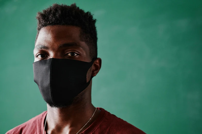 a man wearing a black face mask in front of a green wall, dark skin, schools, all black matte product, on grey background