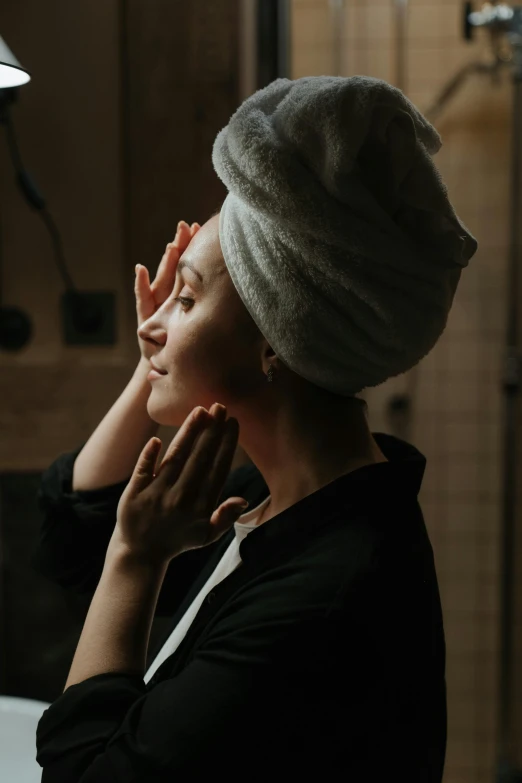 a woman with a towel on her head in a bathroom, pexels contest winner, renaissance, soft light from the side, hands on face, wearing a black robe, skincare