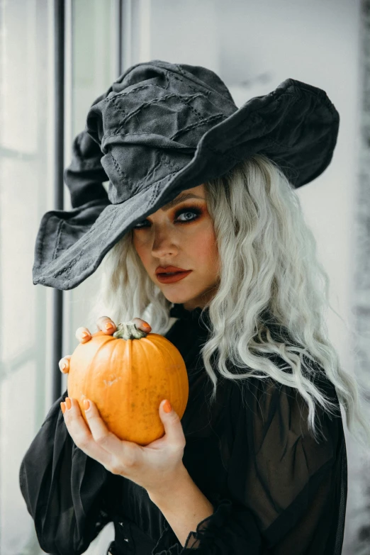 a woman in a witch costume holding a pumpkin, trending on pexels, renaissance, curled silver hair, square, black hat, a blond