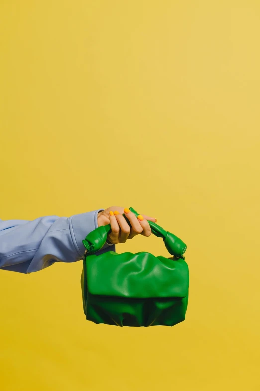 a man holding a green purse on a yellow background, by Adam Saks, trending on pexels, visual art, 🐿🍸🍋, davide sorrenti, green arms, a woman