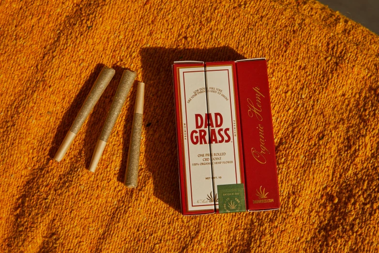 a couple of cigarettes sitting on top of a towel, in a grass field, dad, packaging, red grass