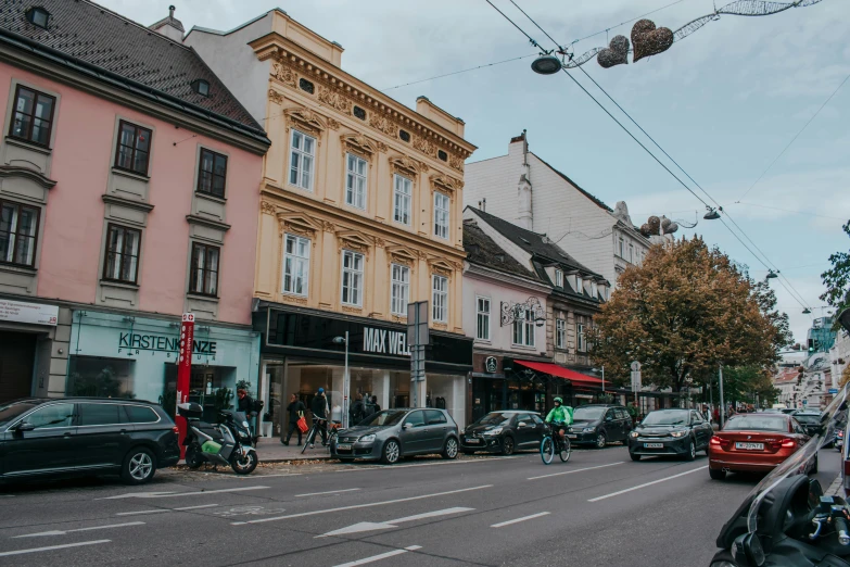 a street filled with lots of traffic next to tall buildings, by Emma Andijewska, pexels contest winner, art nouveau, detmold, shop front, neo - classical, fall season