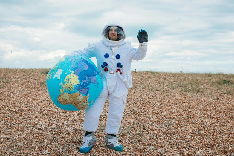 a man in an astronaut suit holding a globe, inspired by Storm Thorgerson, pexels contest winner, dressed as a scavenger, beaches, costume with blue accents, amanda lilleston