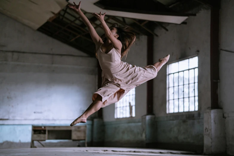 a woman that is jumping in the air, by Elizabeth Polunin, pexels contest winner, arabesque, in a warehouse, lachlan bailey, white, tia masic