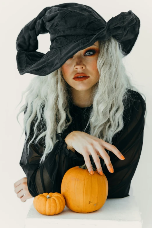 a woman wearing a witch hat and holding two pumpkins, trending on pexels, curled silver hair, gif, black, square