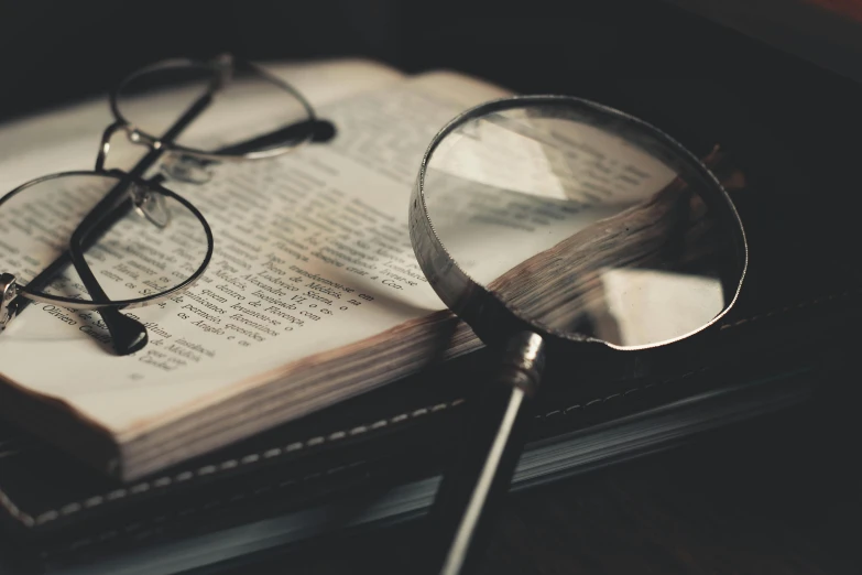 a pair of glasses sitting on top of an open book, a macro photograph, unsplash, photorealism, magnifying glass, dimly - lit, instagram post, detective