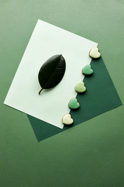 a black leaf sitting on top of a piece of paper, a still life, inspired by Art Green, trending on pexels, environmental art, several hearts, candy decorations, celadon glaze, product introduction photo