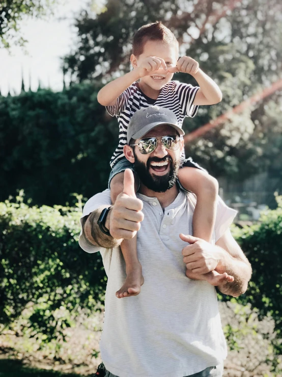 a man holding a little boy on his shoulders, pexels contest winner, wearing sunglasses and a cap, thick black beard, thumb up, 🚿🗝📝