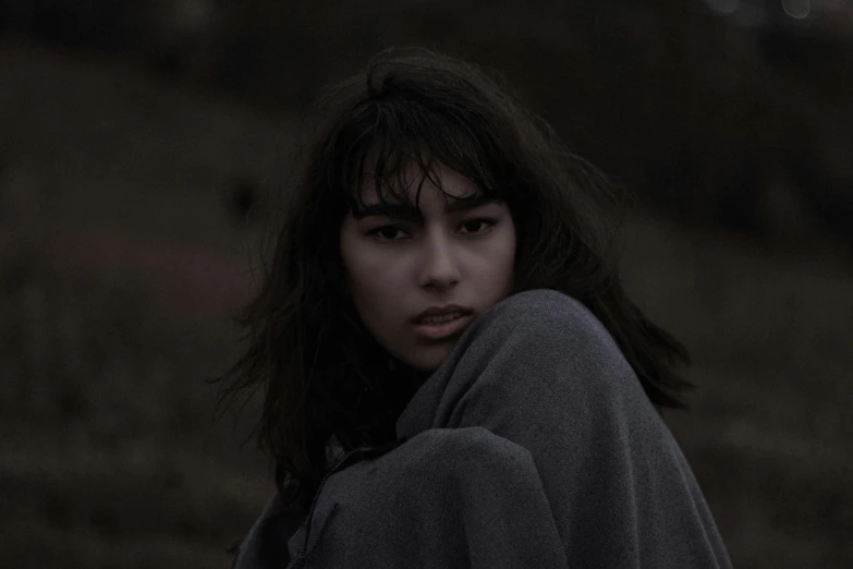 a woman sitting on top of a lush green field, an album cover, inspired by Elsa Bleda, pexels contest winner, underexposed grey, madison beer girl portrait, chilly dark mood, film still from horror movie