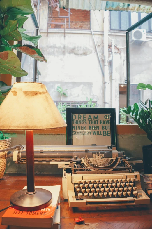 a typewriter sitting on top of a wooden desk next to a lamp, lush plant and magical details, in style of lam manh, saying, a quaint