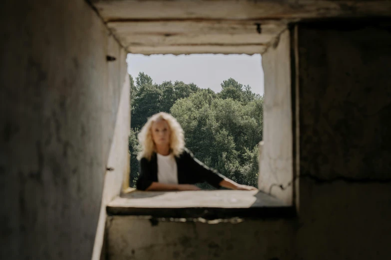 a woman sitting on top of a window sill, an album cover, by Emma Andijewska, pexels contest winner, curly blonde hair | d & d, ruins, view out of a window, ((portrait))