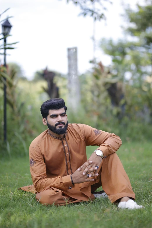 a man sitting on top of a lush green field, an album cover, by Riza Abbasi, pexels contest winner, hurufiyya, wearing tight suit, brown:-2, model posing, photographed for reuters