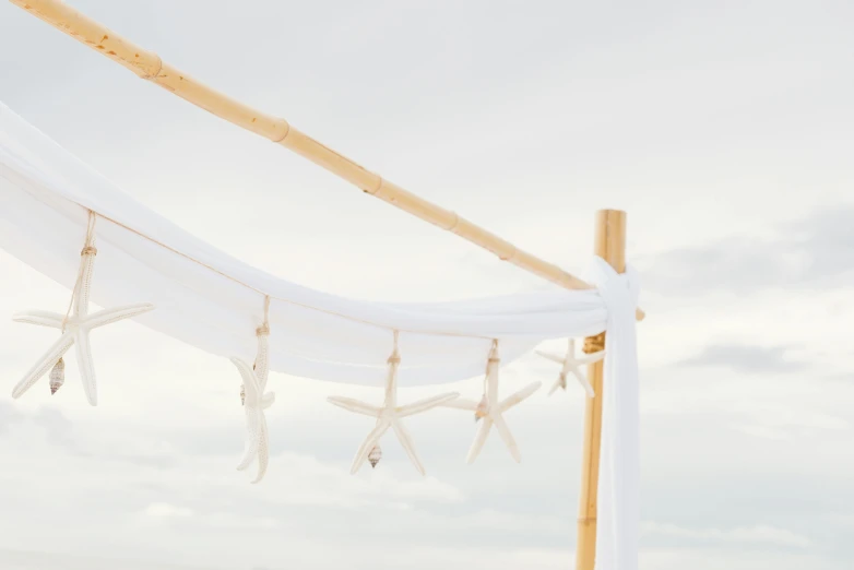 a group of people standing on top of a sandy beach, white cloth, decoration, made of bamboo, starfish