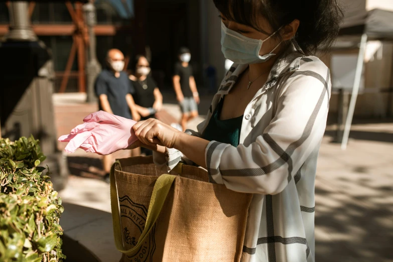 a woman wearing a face mask and holding a shopping bag, by Julia Pishtar, pexels contest winner, strong sunlight, hands on counter, giving gifts to people, people outside eating meals