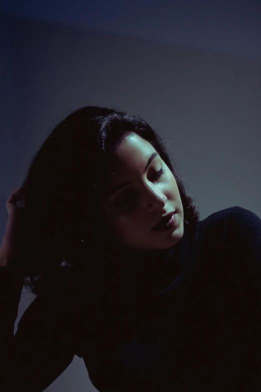 a woman laying on a bed in a dark room, inspired by Elsa Bleda, unsplash, with black hair, profile portrait, concert, on a gray background