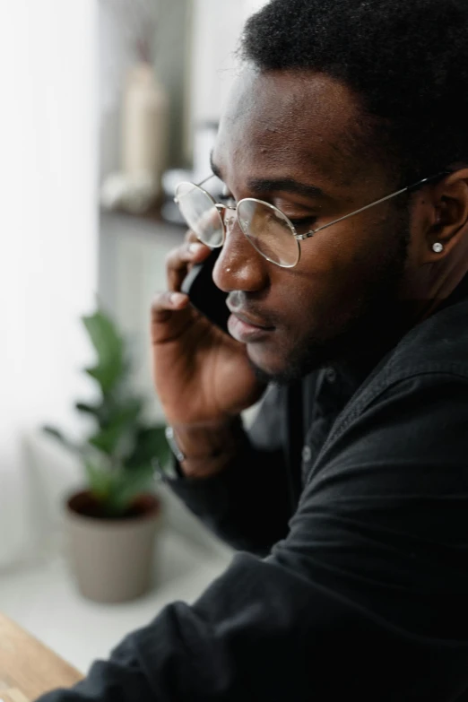 a man sitting at a desk talking on a cell phone, trending on pexels, realism, man is with black skin, man with glasses, pondering, realistic »