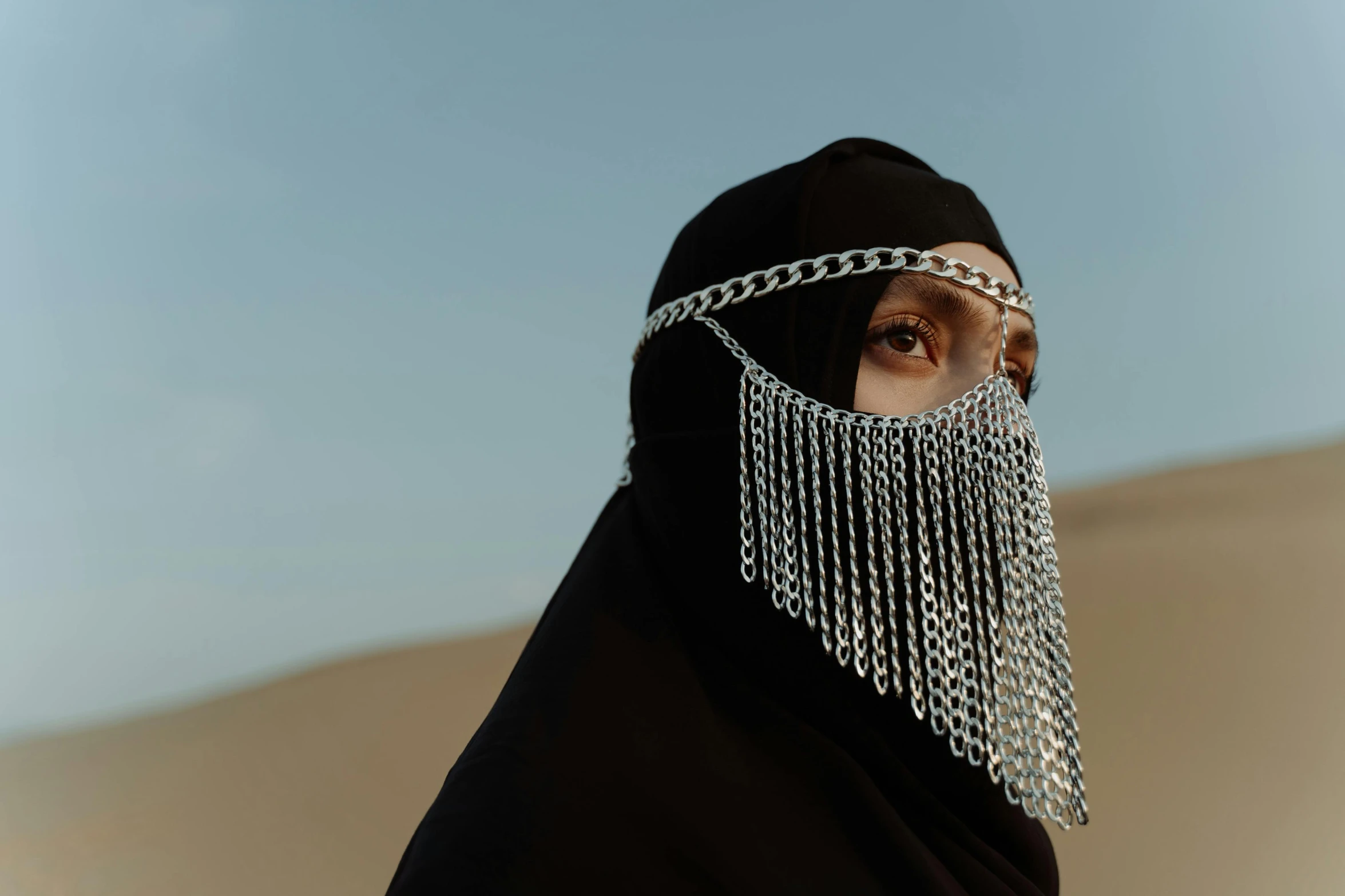 a woman wearing a black hijab in the desert, an album cover, unsplash contest winner, wearing chain mail, face covers half of the frame, cinematic outfit photo, low - angle shot