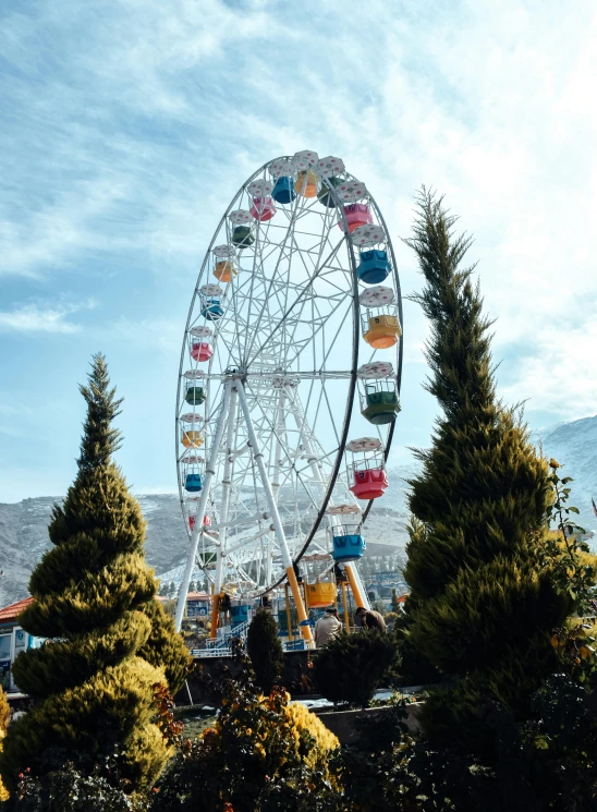 a ferris wheel sitting in the middle of a park, with mountains in the background, winter, high quality product image”