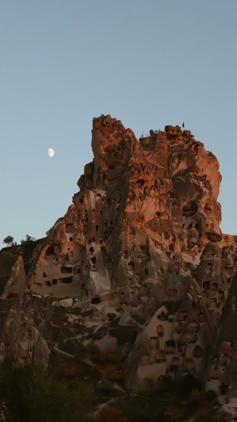 a large rock formation with a moon in the sky, turkey, slide show, multiple stories, cliffside town