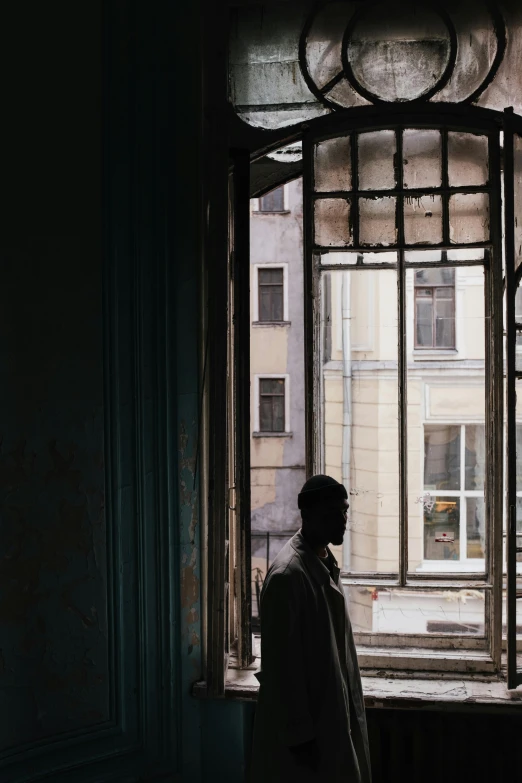 a man standing in front of a window looking out, inspired by Elsa Bleda, pexels contest winner, visual art, post - soviet courtyard, black man, promo image, abandoned building