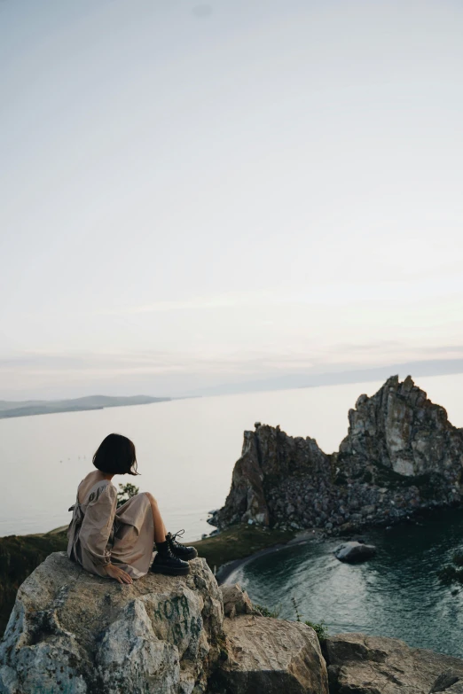 a person sitting on a rock overlooking a body of water, unsplash, romanticism, near lake baikal, wide film still, taliyah, a high angle shot
