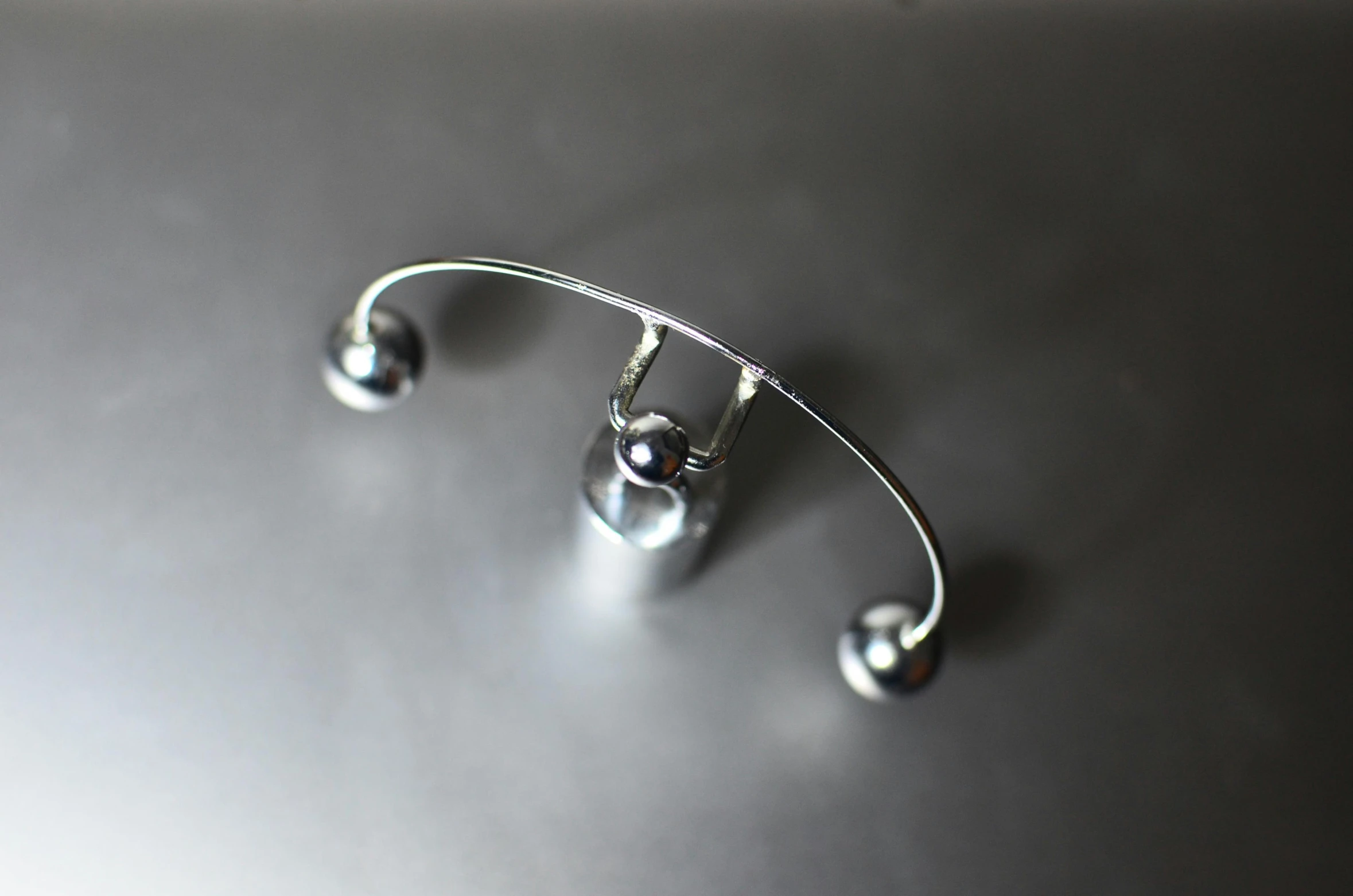 a close up of a metal object on a table, chrome facial piercings, back arched, top down view, hanging