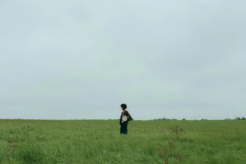 a person standing in a field flying a kite, an album cover, by Attila Meszlenyi, unsplash, conceptual art, movie still 8 k, amelie poulain, overcast, prairie