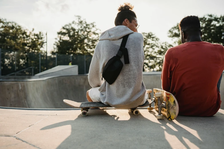 two people sitting on a skateboard at a skate park, trending on pexels, her back is to us, lifestyle, half image, looking her shoulder