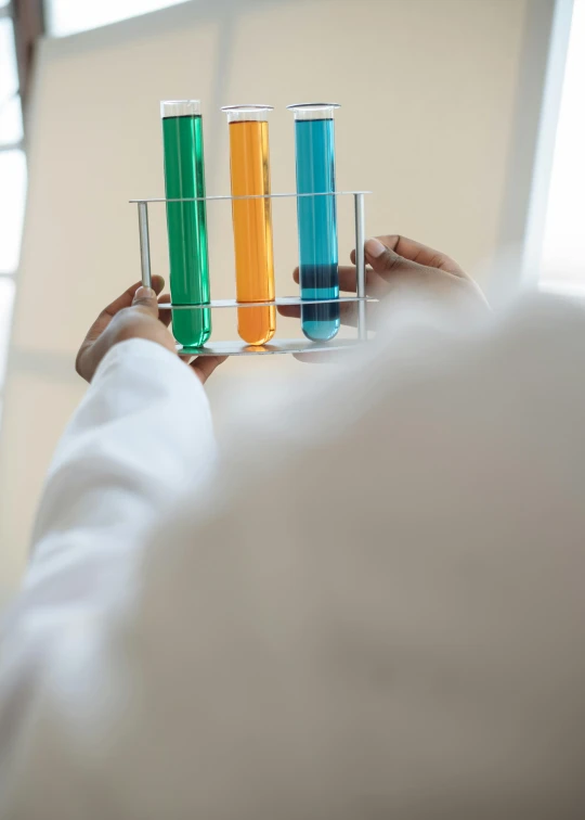 a person holding a glass filled with colored liquid, test tubes, promo image, white lab coat, pillars